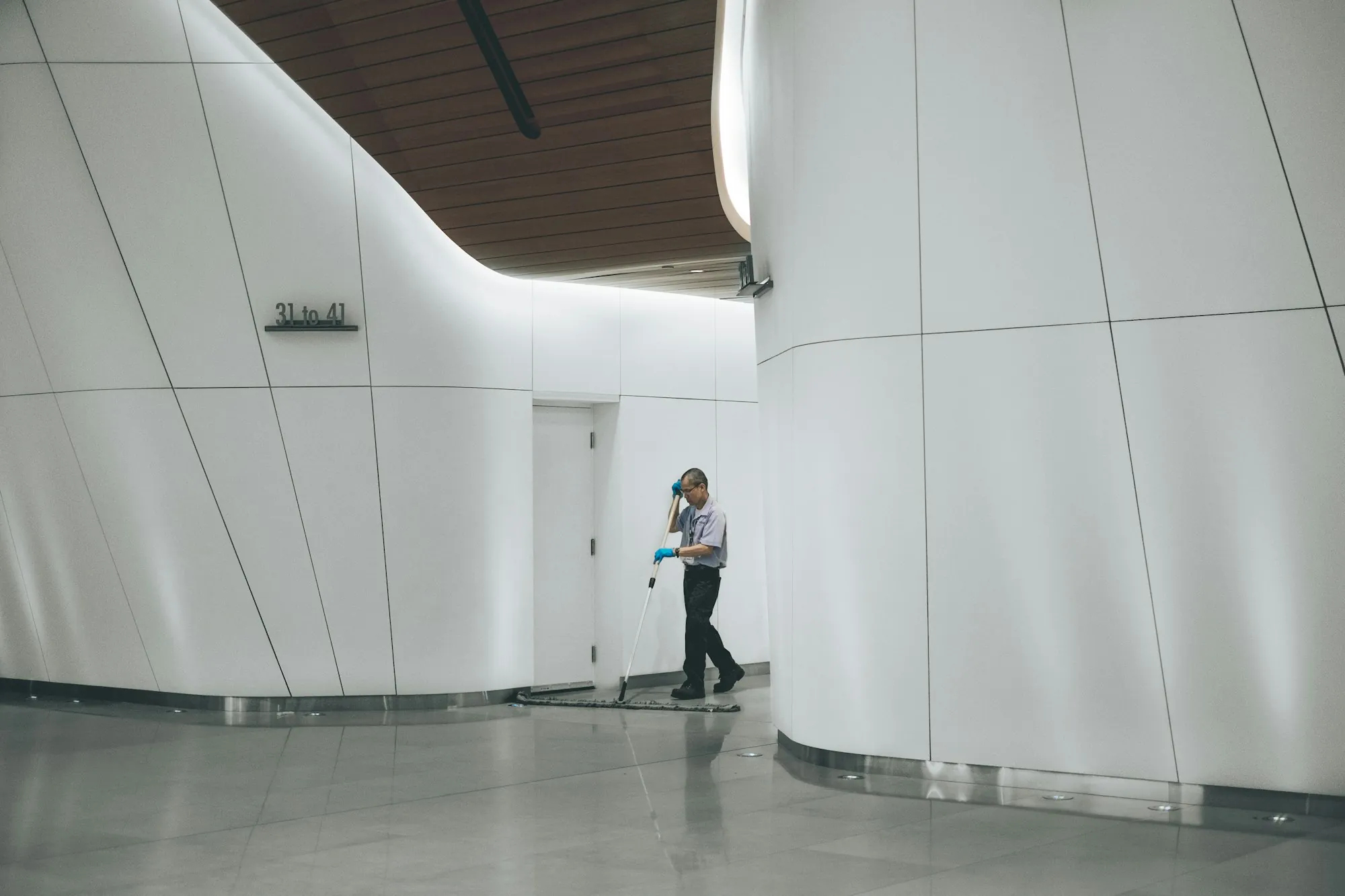 Janitor mopping a polished floor in a modern curved hallway